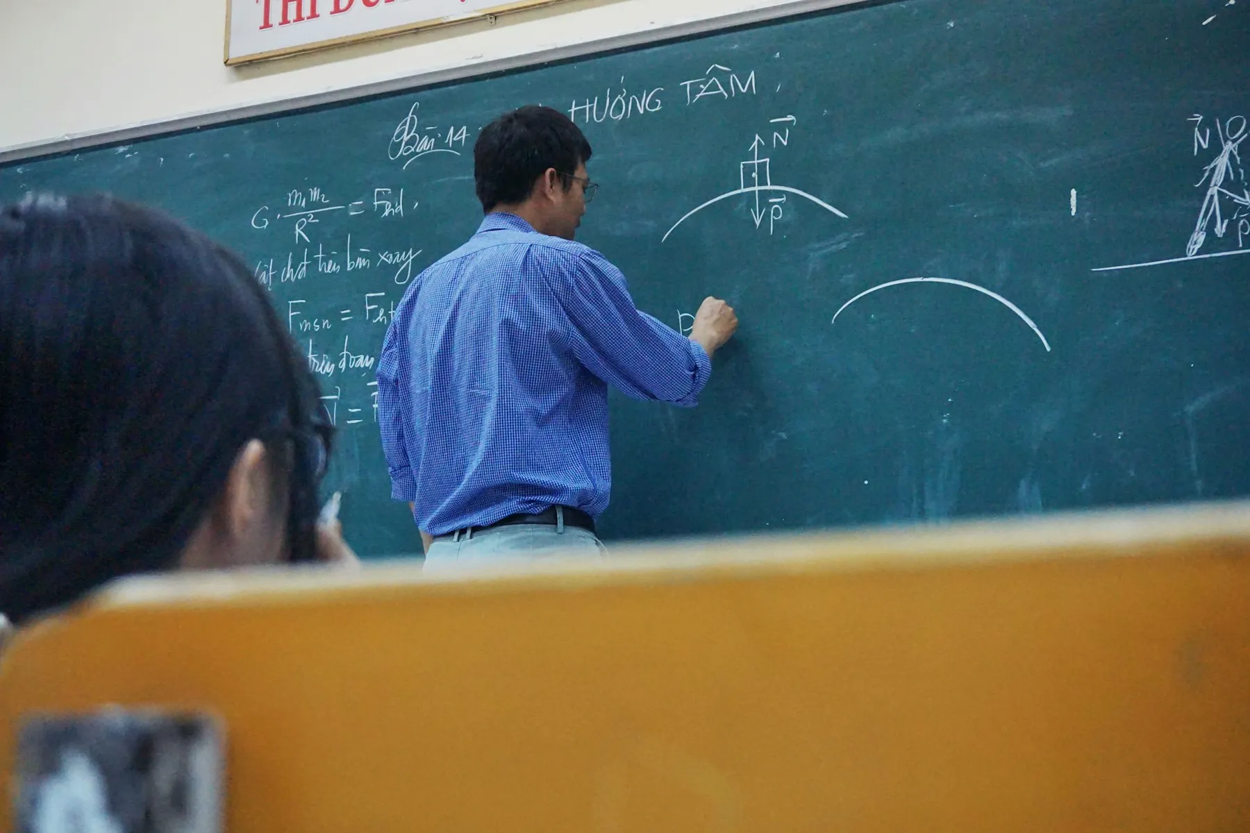 A teacher explaining physics at a chalkboard.